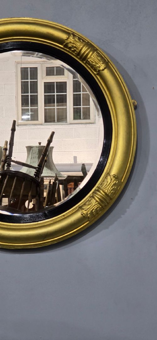 A circular Regency style giltwood mirror featuring a black inner reeded slip and classical acanthus leaf decorative accents on the moulded frame. View III