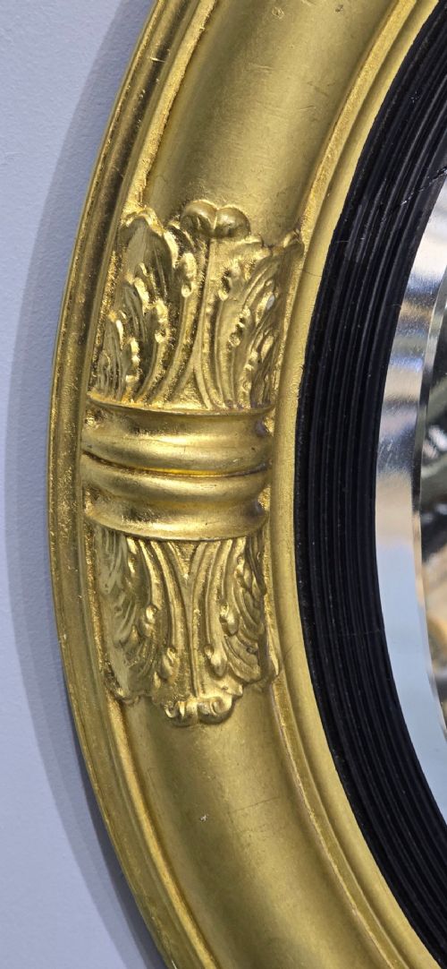 A circular Regency style giltwood mirror featuring a black inner reeded slip and classical acanthus leaf decorative accents on the moulded frame. View IV