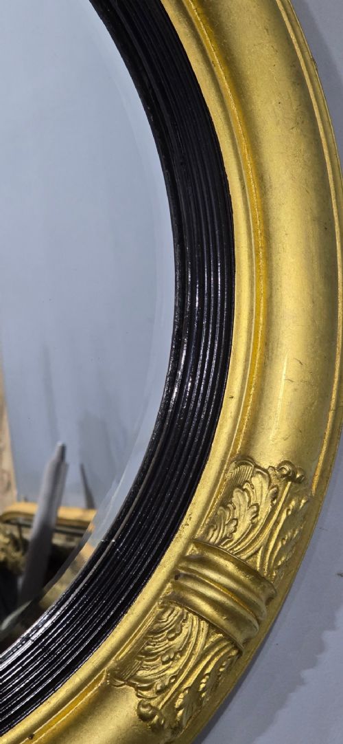 A circular Regency style giltwood mirror featuring a black inner reeded slip and classical acanthus leaf decorative accents on the moulded frame. View V