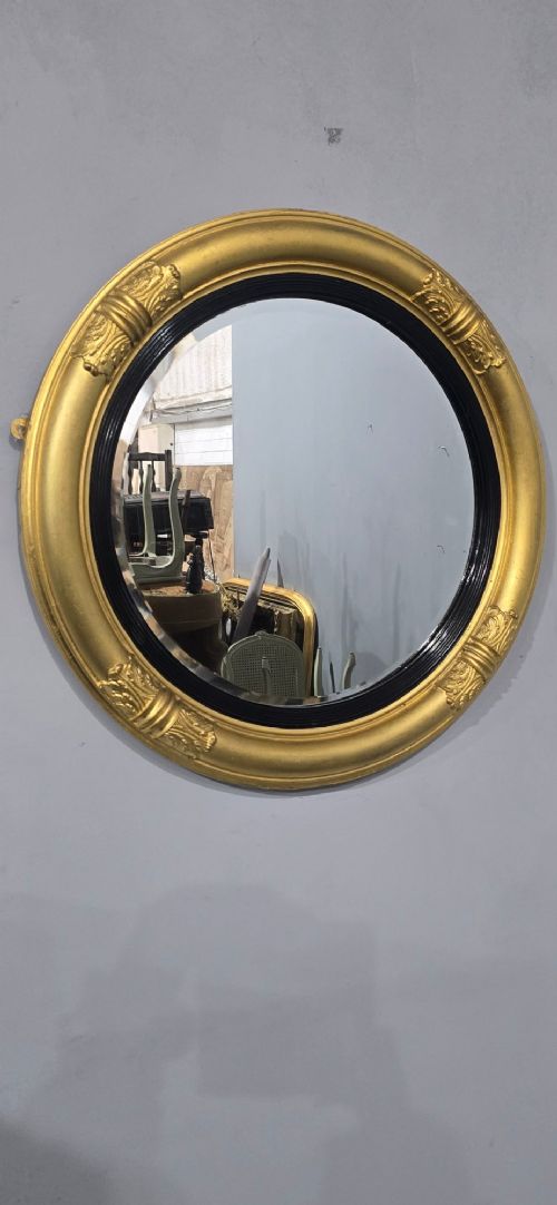A circular Regency style giltwood mirror featuring a black inner reeded slip and classical acanthus leaf decorative accents on the moulded frame. View VI