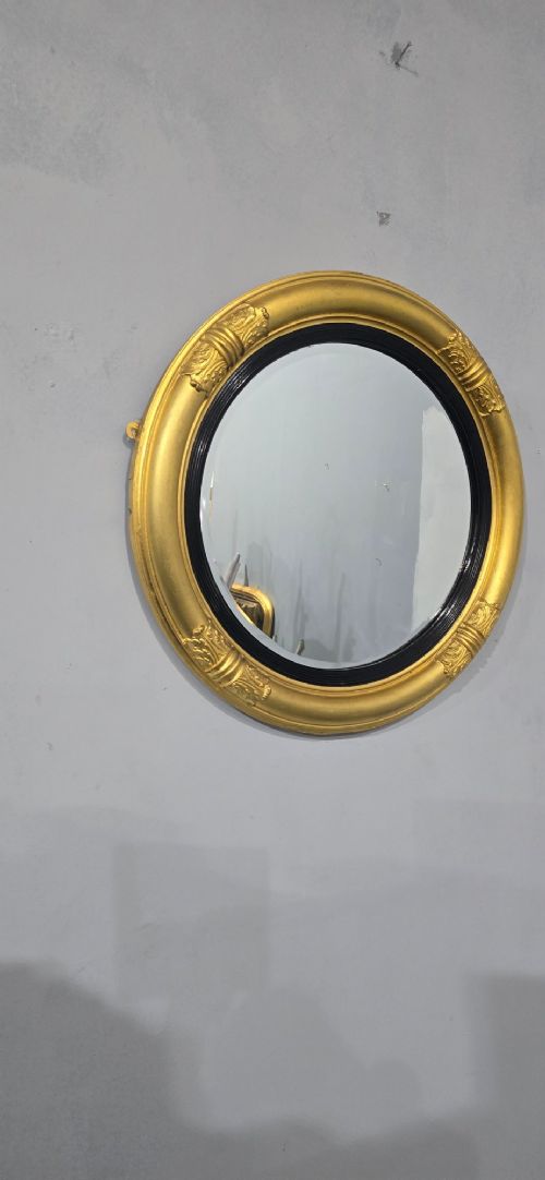 A circular Regency style giltwood mirror featuring a black inner reeded slip and classical acanthus leaf decorative accents on the moulded frame. View VII