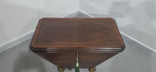 fig 1. A tapered sarcophagus-shaped dark mahogany wine cooler featuring satinwood line inlay, brass lion paw feet, and a central keyhole with a green tassel.