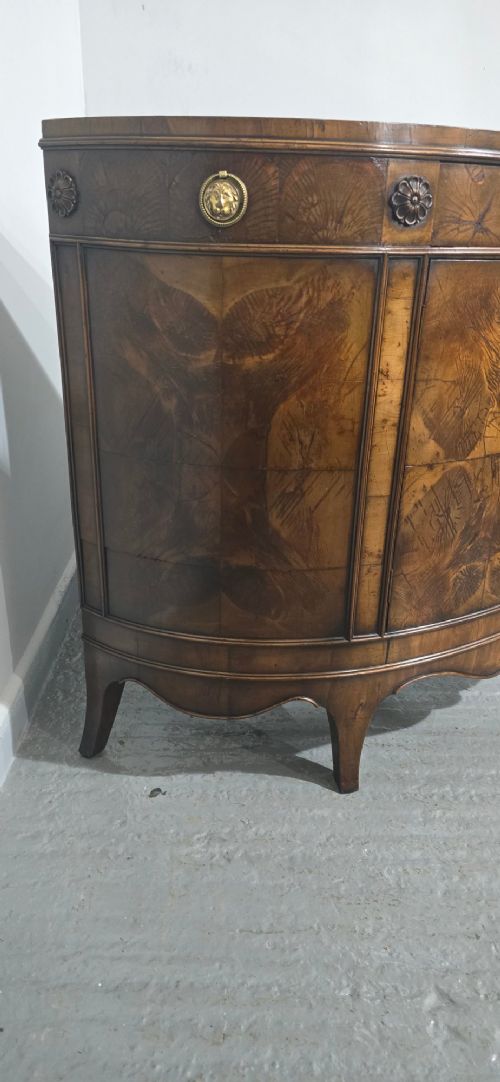 A semi-circular burr yew wood side cabinet featuring brass mounts along the frieze and central double doors. View III
