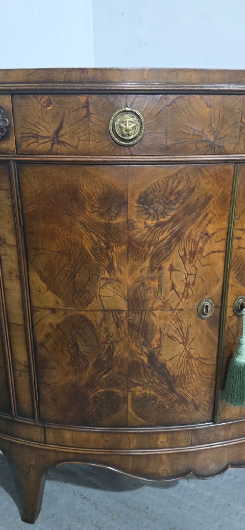 A semi-circular burr yew wood side cabinet featuring brass mounts along the frieze and central double doors. View VI