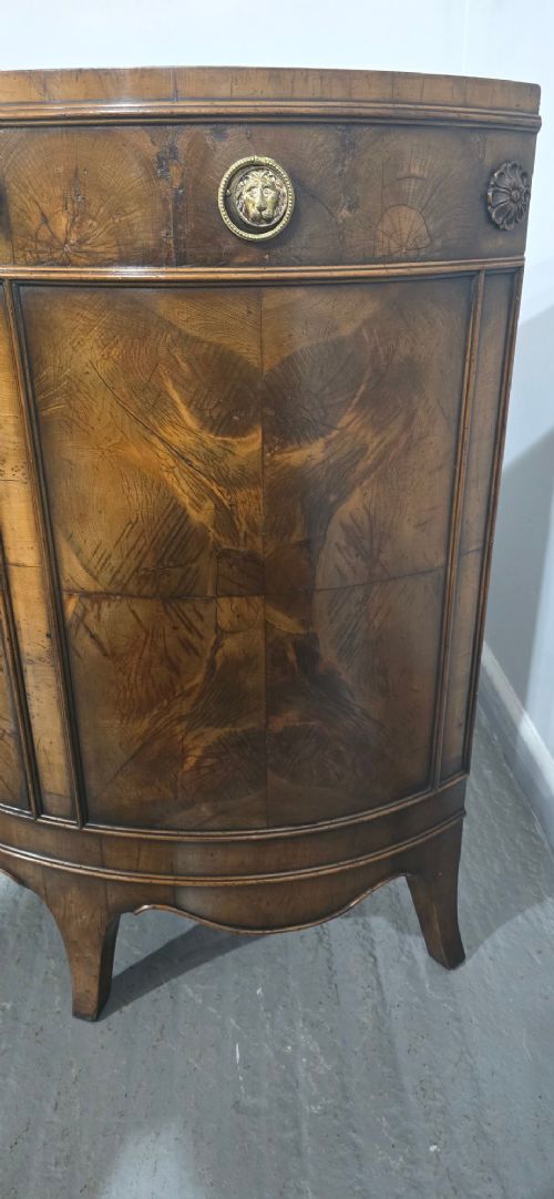 A semi-circular burr yew wood side cabinet featuring brass mounts along the frieze and central double doors. View VII