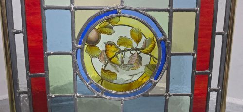 fig 1. A brass fire screen featuring a leaded stained glass panel with a central hand-painted bird roundel set on splayed brass feet.