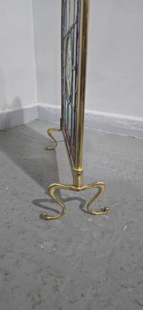 A brass fire screen featuring a leaded stained glass panel with a central hand-painted bird roundel set on splayed brass feet. View IV