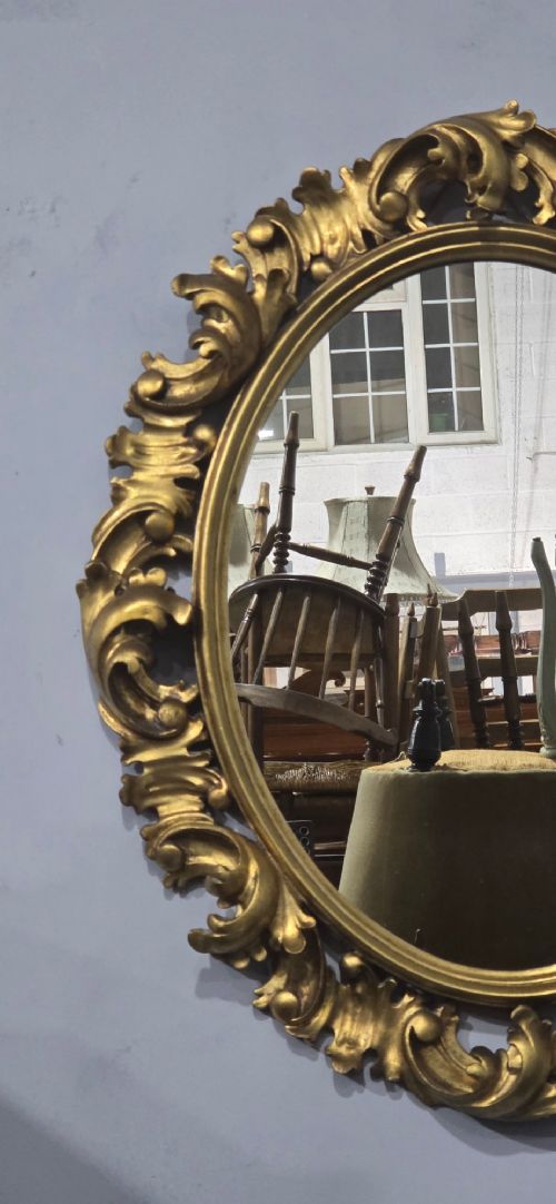 An oval wall mirror enclosed in a deeply carved gold giltwood frame featuring ornate acanthus leaf and scrolling foliage details. View III