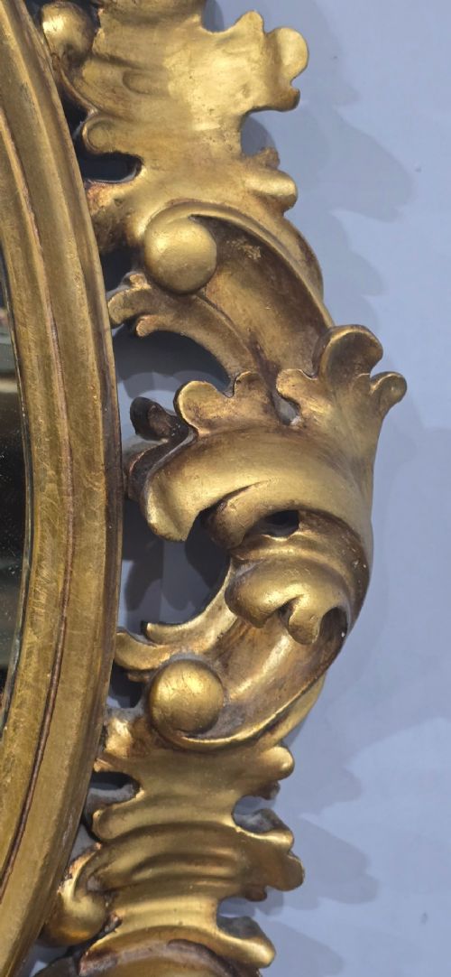 An oval wall mirror enclosed in a deeply carved gold giltwood frame featuring ornate acanthus leaf and scrolling foliage details. View XII