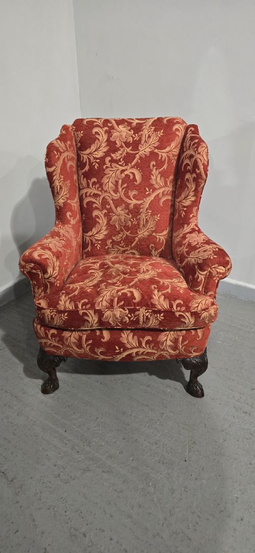 fig 1. A high-backed wing armchair upholstered in red floral damask fabric with carved mahogany cabriole front legs featuring claw and ball feet.