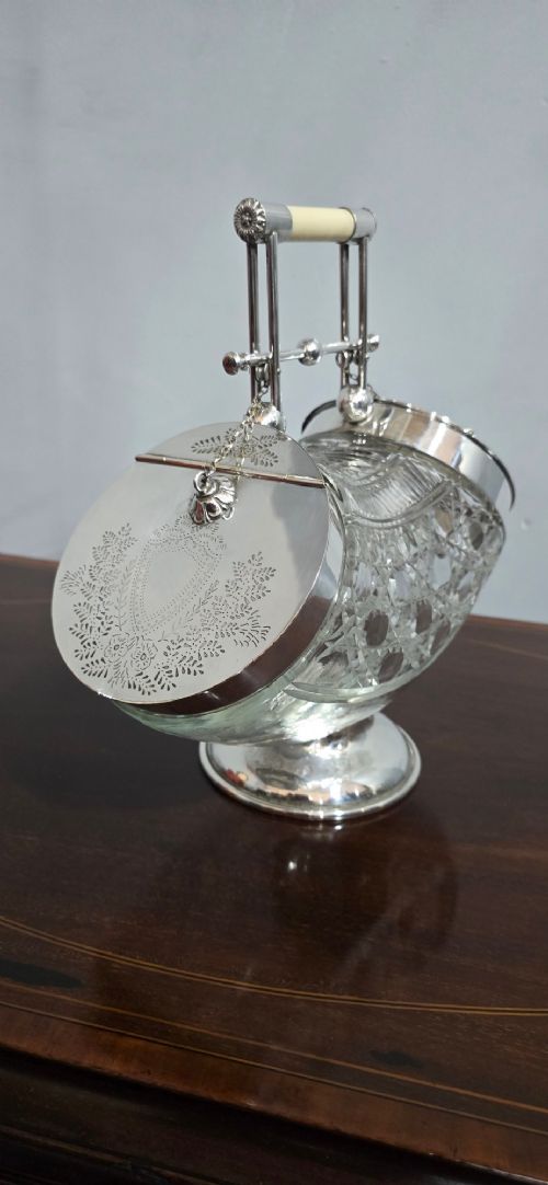 fig 1. An Edwardian cut glass biscuit barrel featuring a hobnail geometric pattern, silver-plated frame, overhead handle, and pedestal base.