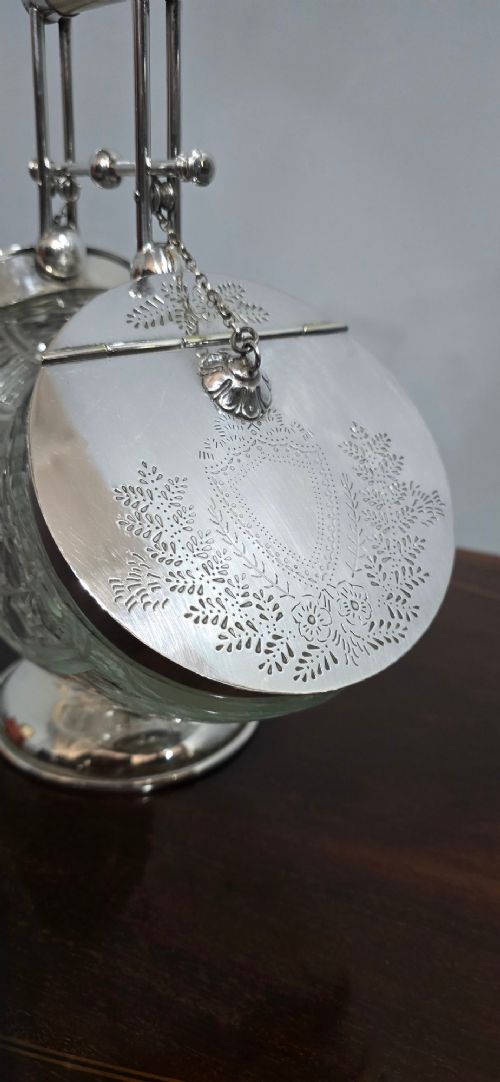 An Edwardian cut glass biscuit barrel featuring a hobnail geometric pattern, silver-plated frame, overhead handle, and pedestal base. View V