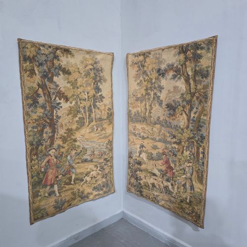 fig 1. A pair of vertical woven French tapestries depicting men and hounds hunting within a dense green forest and natural landscape.