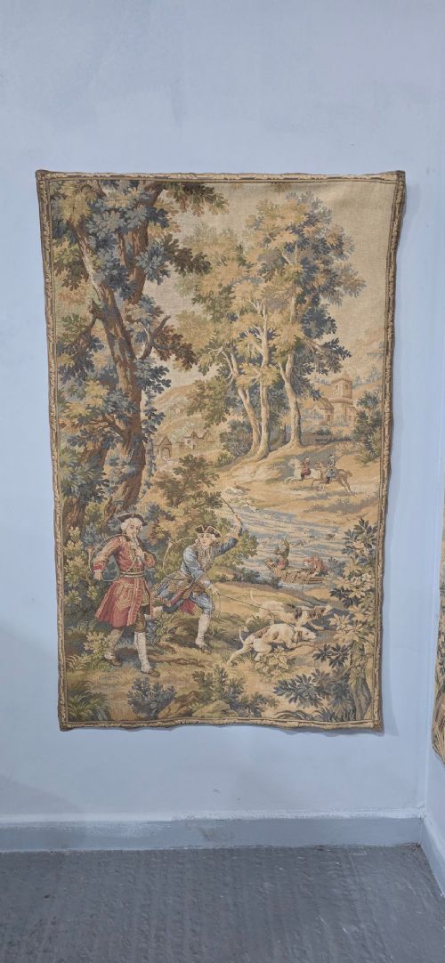 A pair of vertical woven French tapestries depicting men and hounds hunting within a dense green forest and natural landscape. View III