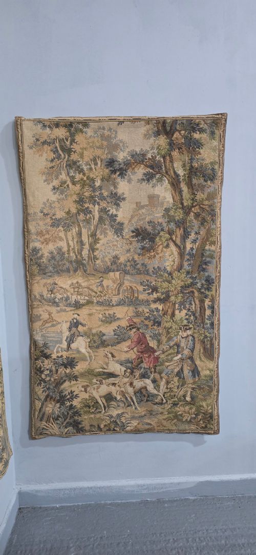 A pair of vertical woven French tapestries depicting men and hounds hunting within a dense green forest and natural landscape. View IV