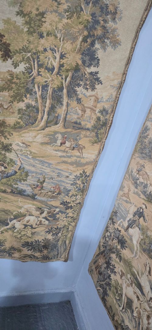 A pair of vertical woven French tapestries depicting men and hounds hunting within a dense green forest and natural landscape. View V