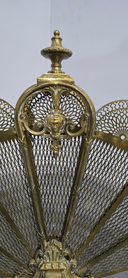 An ornate Victorian brass peacock fire screen featuring pierced filigree fan panels, a finial crest, and a cast scrollwork base. View VI