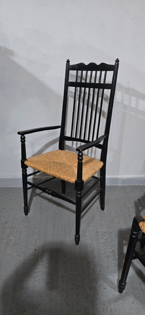 A set of eight Arts and Crafts ebonised wooden dining chairs featuring high spindle backs and hand-woven natural rush seats. View V