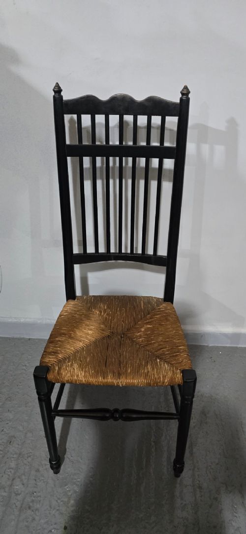 A set of eight Arts and Crafts ebonised wooden dining chairs featuring high spindle backs and hand-woven natural rush seats. View VIII