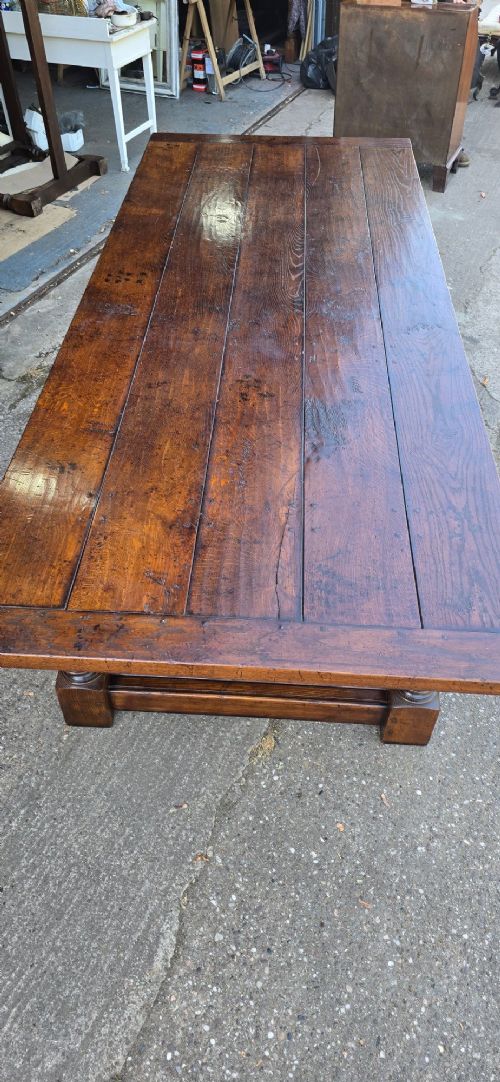 A large solid oak refectory dining table featuring a wide plank top, breadboard ends, turned baluster legs, and a low H-stretcher base. View VII