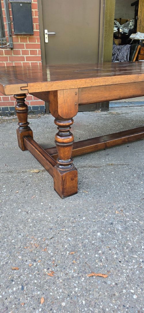 A large solid oak refectory dining table featuring a wide plank top, breadboard ends, turned baluster legs, and a low H-stretcher base. View IX