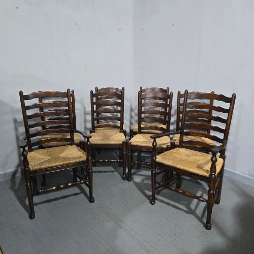 fig 1. A set of eight dark oak ladder back dining chairs featuring woven rush seats, curved back rungs, and turned front legs with stretchers.