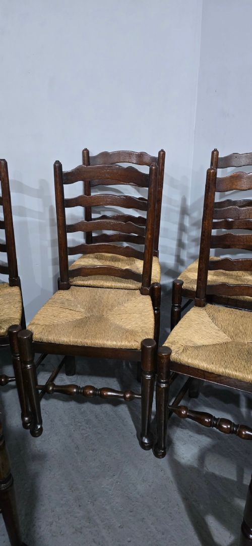 A set of eight dark oak ladder back dining chairs featuring woven rush seats, curved back rungs, and turned front legs with stretchers. View V