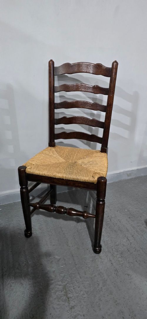 A set of eight dark oak ladder back dining chairs featuring woven rush seats, curved back rungs, and turned front legs with stretchers. View IX