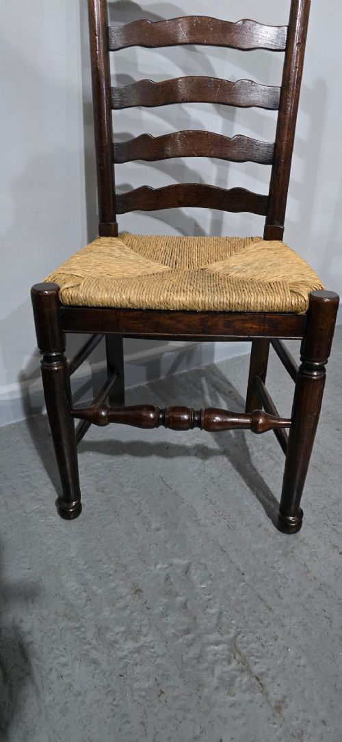 A set of eight dark oak ladder back dining chairs featuring woven rush seats, curved back rungs, and turned front legs with stretchers. View X