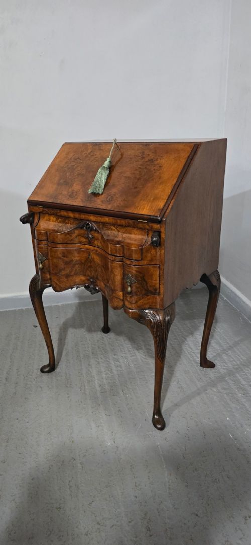fig 1. A Queen Anne style burr walnut writing bureau featuring a sloped front lid, shaped drawers with brass drop handles, and tall cabriole legs.