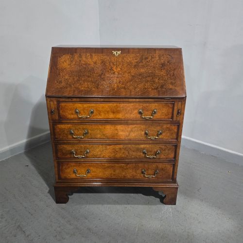 fig 1. An antique Queen Anne burr walnut writing bureau featuring a sloping fall-front lid over four graduated drawers with brass drop handles and bracket feet.