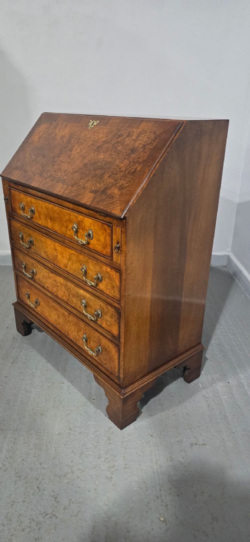 An antique Queen Anne burr walnut writing bureau featuring a sloping fall-front lid over four graduated drawers with brass drop handles and bracket feet. View VII