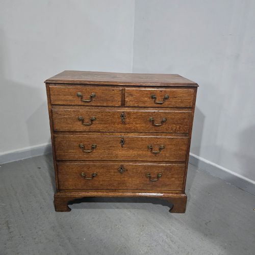fig 1. A Georgian oak chest of drawers featuring two short drawers above three long graduated drawers with brass swan-neck handles and bracket feet.