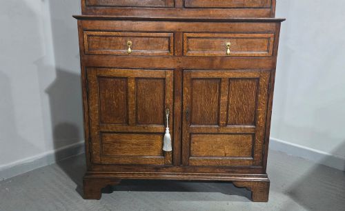 fig 1. A dark oak Georgian court cupboard featuring an upper cabinet with arched panel doors, two central drawers, and a lower double-door cupboard on bracket feet.