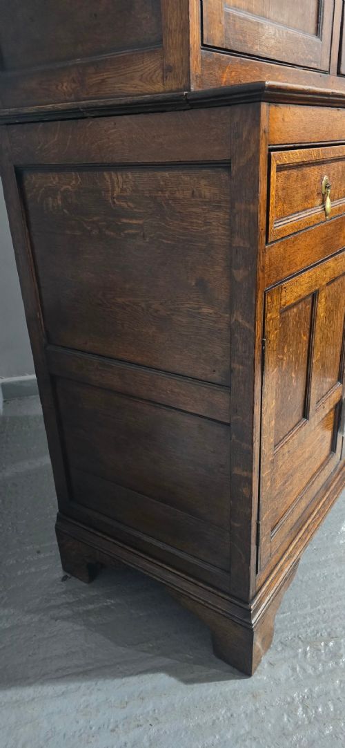 A dark oak Georgian court cupboard featuring an upper cabinet with arched panel doors, two central drawers, and a lower double-door cupboard on bracket feet. View X