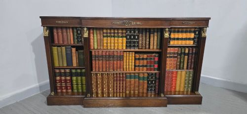fig 1. An antique Empire style breakfront low mahogany bookcase featuring three sections of open adjustable shelves filled with books and adorned with gilt bronze mounts and fluted pilasters.