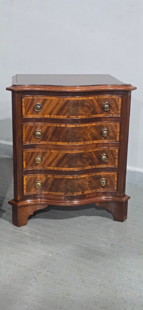 A matching pair of serpentine-fronted mahogany bedside chests, each featuring four drawers with inlay crossbanding and circular brass ring handles. View V