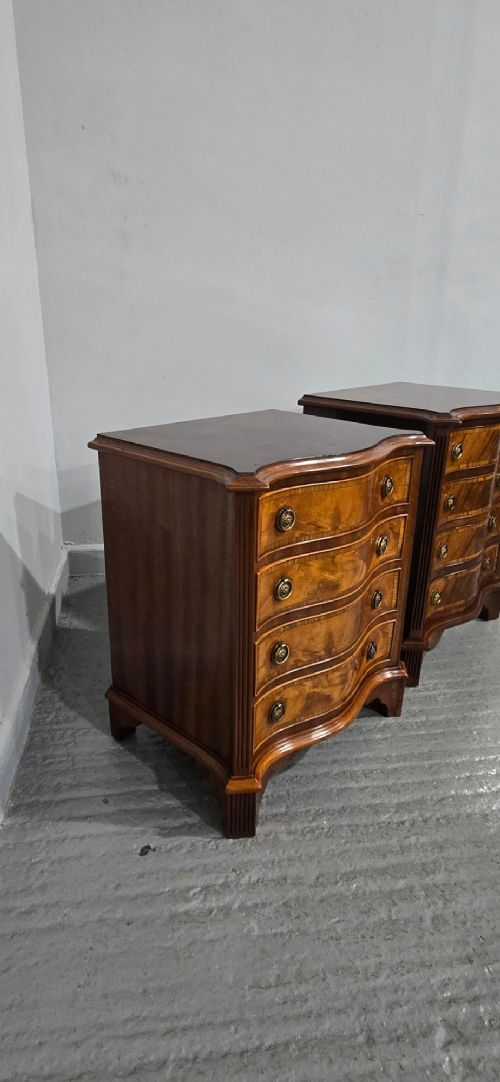 A matching pair of serpentine-fronted mahogany bedside chests, each featuring four drawers with inlay crossbanding and circular brass ring handles. View X