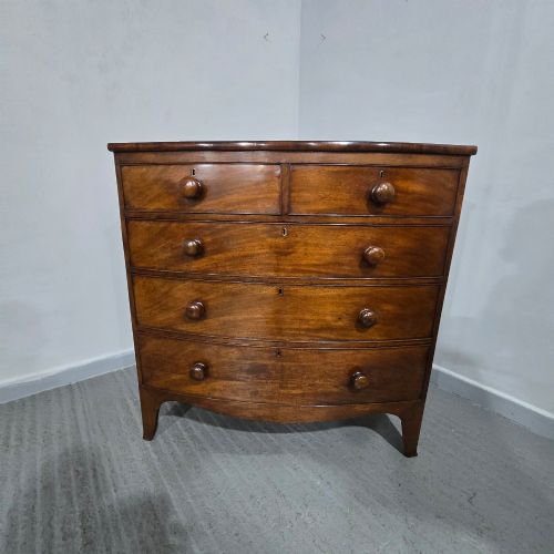 fig 1. An antique mahogany bow-front chest of drawers featuring two short drawers over three long graduated drawers with turned wooden knobs.