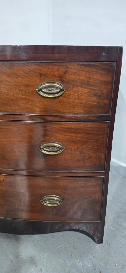 An antique Georgian mahogany bowfront chest featuring three drawers with oval brass handles and keyholes. View V