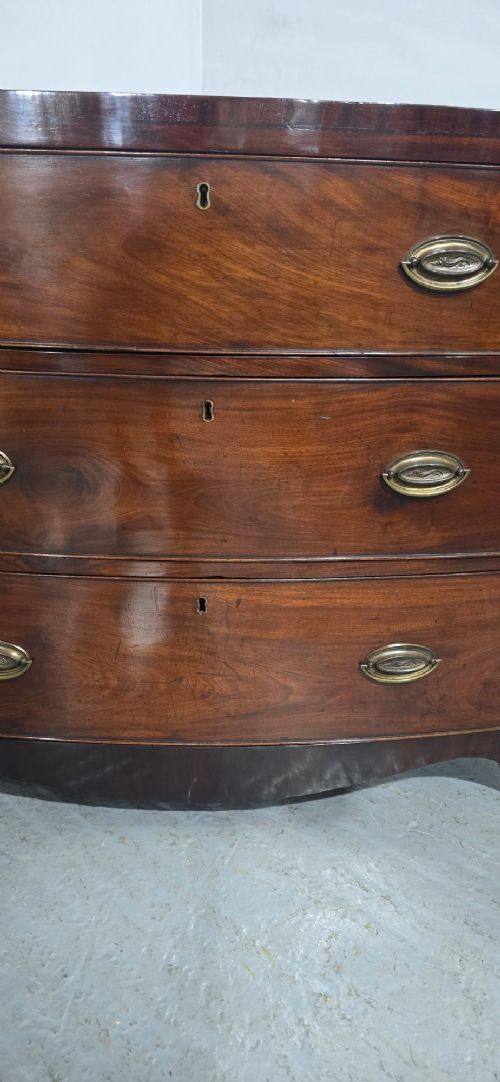 An antique Georgian mahogany bowfront chest featuring three drawers with oval brass handles and keyholes. View VI
