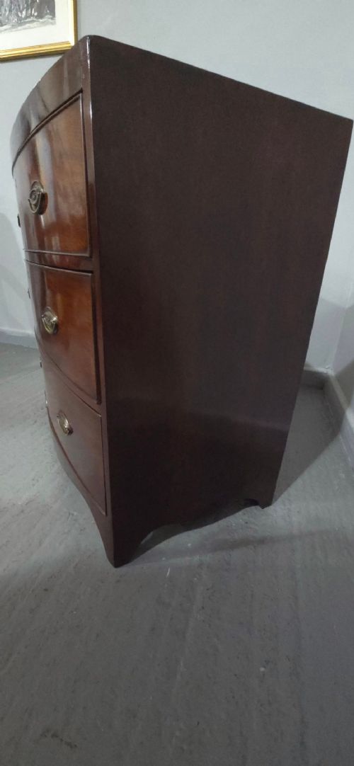 An antique Georgian mahogany bowfront chest featuring three drawers with oval brass handles and keyholes. View IX
