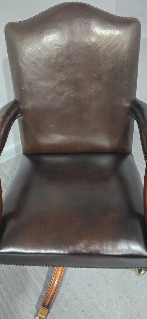 A dark brown leather upholstered swivel desk chair featuring carved mahogany armrests, brass studding, and splayed legs with brass castors. View V