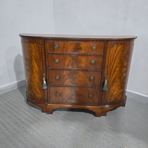 fig 1. A mahogany bowfront sideboard featuring four central drawers flanked by two curved outer cupboard doors with flame mahogany veneer panels and brass ring handles.