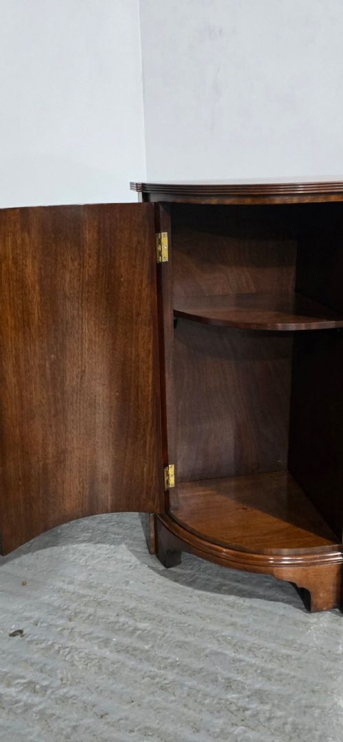 A mahogany bowfront sideboard featuring four central drawers flanked by two curved outer cupboard doors with flame mahogany veneer panels and brass ring handles. View VII