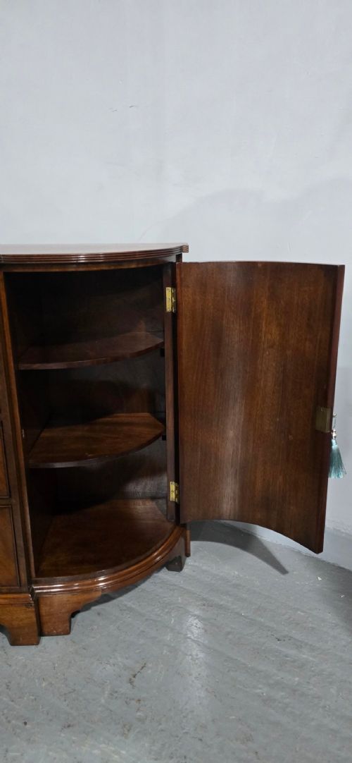 A mahogany bowfront sideboard featuring four central drawers flanked by two curved outer cupboard doors with flame mahogany veneer panels and brass ring handles. View VIII