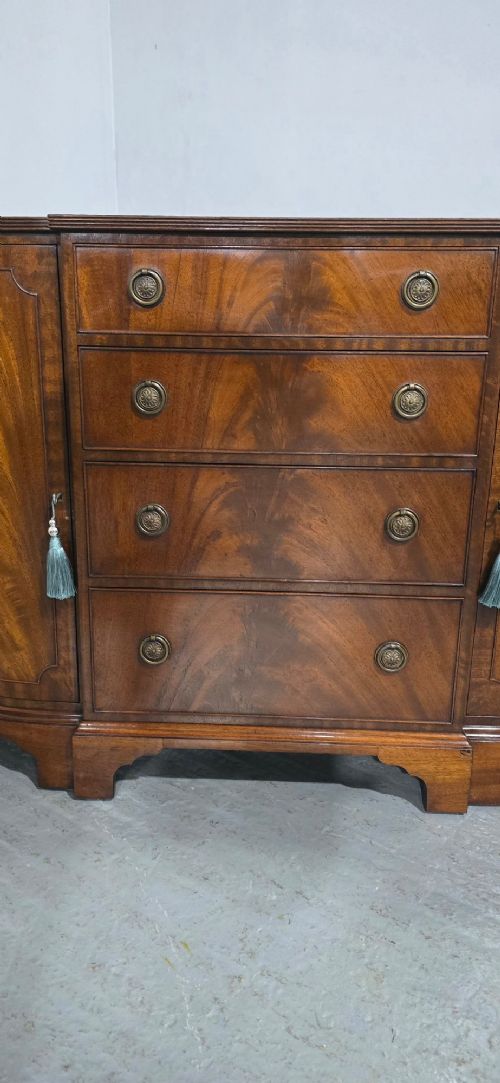 A mahogany bowfront sideboard featuring four central drawers flanked by two curved outer cupboard doors with flame mahogany veneer panels and brass ring handles. View X
