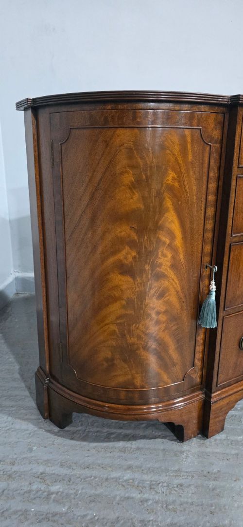 A mahogany bowfront sideboard featuring four central drawers flanked by two curved outer cupboard doors with flame mahogany veneer panels and brass ring handles. View XI