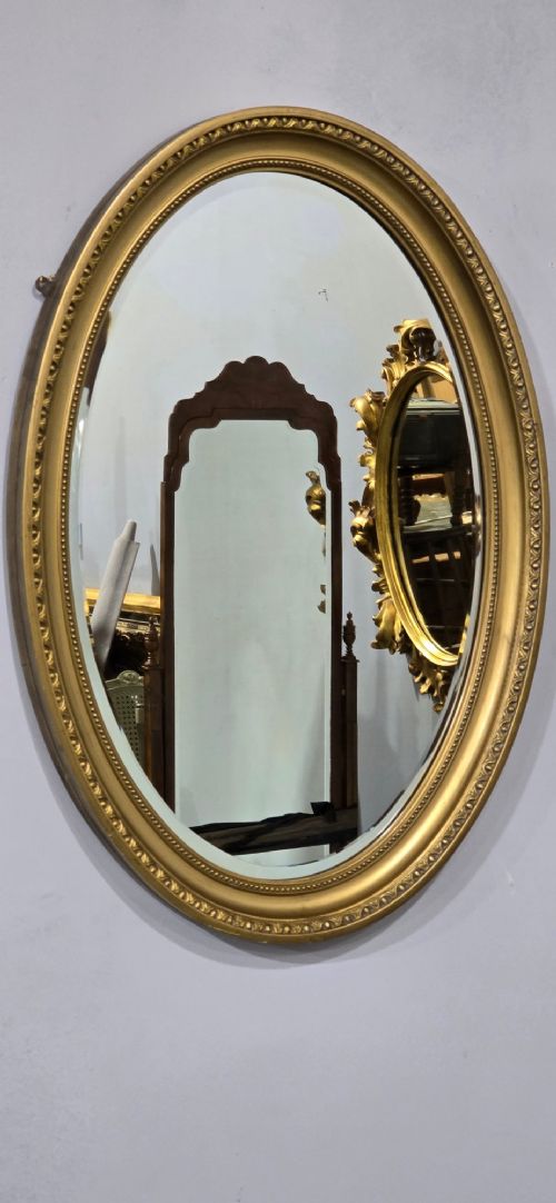fig 1. An antique oval wall mirror featuring a gilded frame decorated with beaded and egg-and-dart moulded trim.