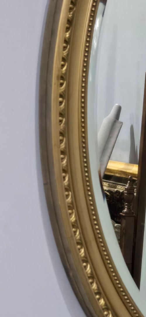 An antique oval wall mirror featuring a gilded frame decorated with beaded and egg-and-dart moulded trim. View III